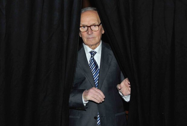 Ennio Morricone is standing between black curtains wearing a suit and striped tie, 2K Desktop Wallpaper