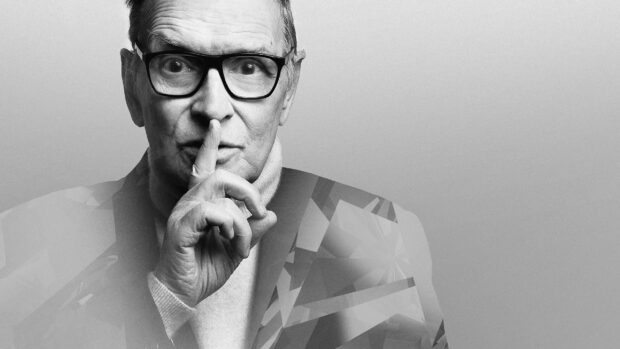 Ennio Morricone Wallpapers showing a man with glasses making a silence gesture, 2K Desktop Wallpaper