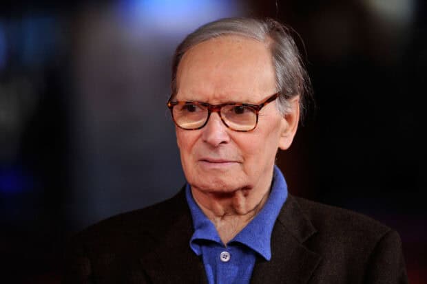Ennio Morricone is shown wearing glasses and a blue shirt with a dark jacket, HD Desktop Wallpaper