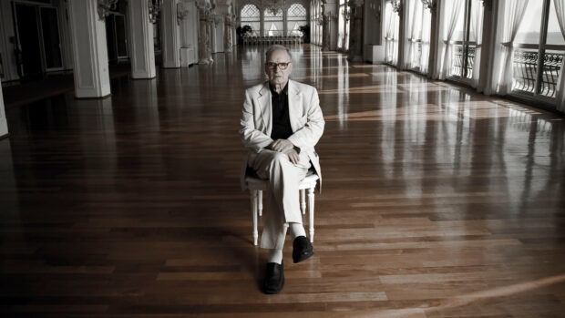 Ennio Morricone sits in a spacious hall with wooden floors and large windows, HD Desktop Wallpaper