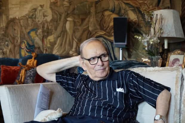 Ennio Morricone is sitting comfortably on a couch in a decorated room, 2K Desktop Wallpaper