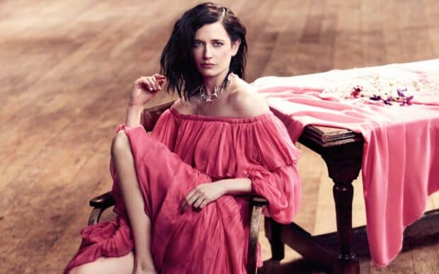 Eva Green is seated wearing a flowing pink dress indoors near a wooden table with flowers, HD Desktop Wallpaper