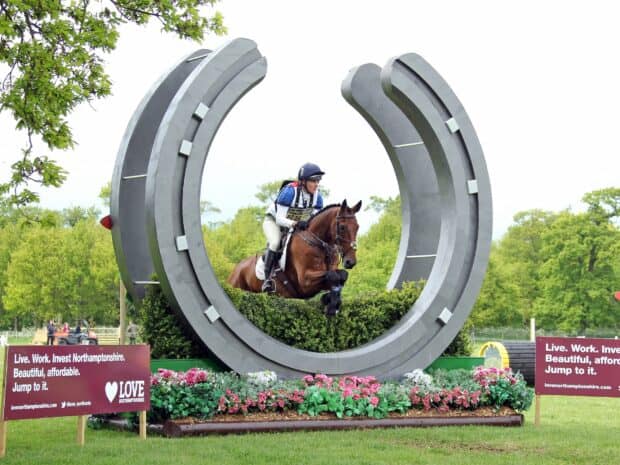 A rider on a horse clears a large horseshoe shaped obstacle during an eventing competition, HD Desktop Wallpaper