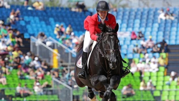 A rider in a red jacket is jumping a black horse during eventing with a crowd in the background, HD Desktop Wallpaper