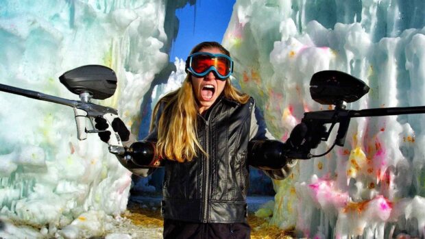 A paintball player is holding two guns in front of icy formations, HD Desktop Wallpaper