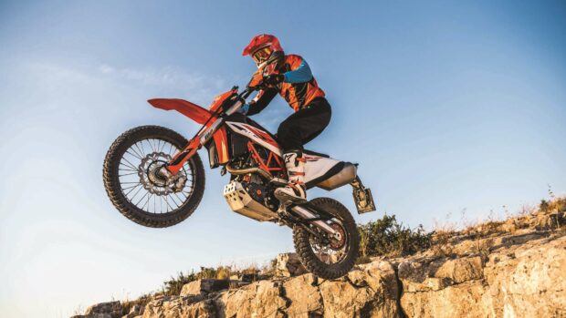 A rider on an enduro motorbike jumps over rocky cliffs under a clear blue sky, 4K Desktop Wallpaper