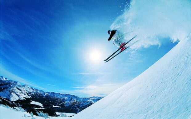 A skier performs a jump down a snowy mountain on a clear day with blue sky and sun, HD Desktop Wallpaper