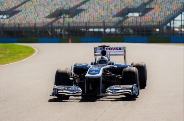 A Formula 1 race car is driving fast on a racetrack with a colorful grandstand in the background, HD Desktop Wallpaper