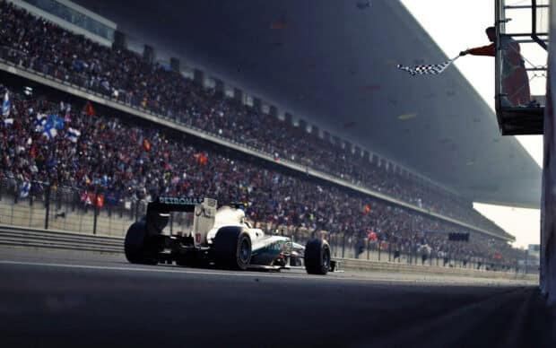 An F1 race car speeds past the finish line with the crowd cheering loudly, HD Desktop Wallpaper