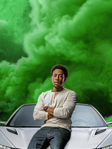 A man is standing confidently in front of a sports car with green smoke behind him in F9 wallpapers, 2K Desktop Wallpaper