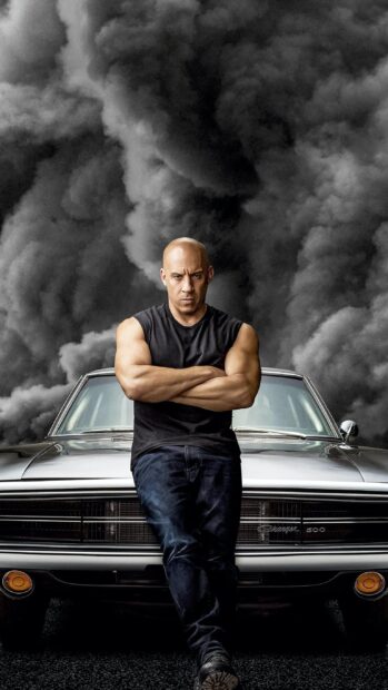 A muscular man stands confidently in front of a vintage car with smoke in the background featuring F9 Wallpapers, 2K Phone Wallpaper