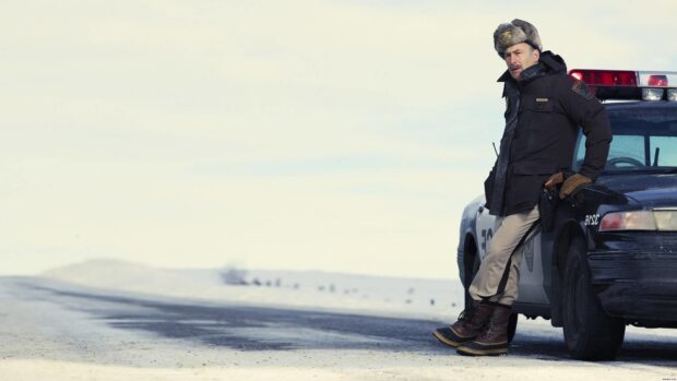 A man in winter clothing leans on a police car in a snowy landscape with Fargo wallpapers, HD Desktop Wallpaper