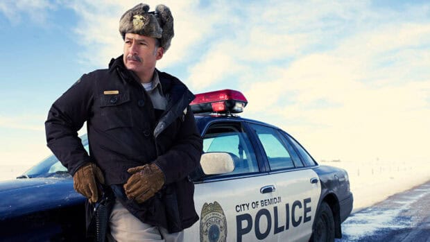A Fargo police officer wearing a winter hat stands beside a patrol car in a snowy landscape, HD Desktop Wallpaper
