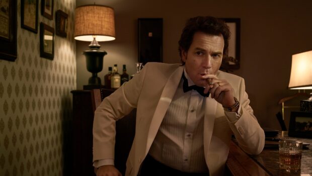 A man in a beige suit smokes a cigar while sitting at a desk in a dimly lit room with lamps, 4K Desktop Wallpaper