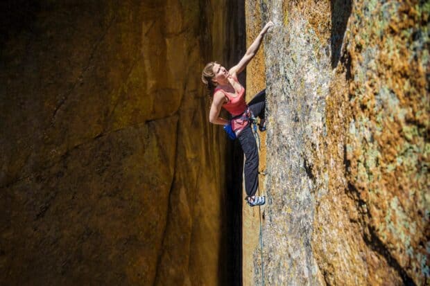 A woman is focused on her climb while scaling a textured rock wall during a rock climbing adventure, HD Desktop Wallpaper