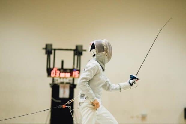 A fencer wearing protective gear is engaged in a bout with a foil sword during a competition, 2K Desktop Wallpaper