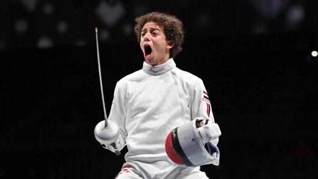 A fencing athlete wearing white gear celebrates during a competition with a sword and helmet in hand, 2K Desktop Wallpaper