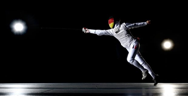 A fencing athlete lunges forward with an extended arm holding a sword during a match, 2K Desktop Wallpaper