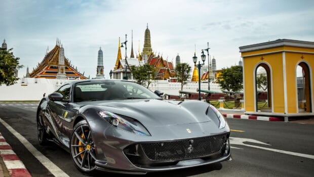 A sleek gray Ferrari 812 Gts parked by the roadside with ornate temple structures in the background