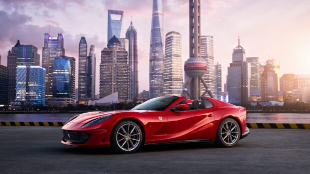 A red Ferrari 812 Gts is parked with a city skyline at sunset in the background, 4K Desktop Wallpaper