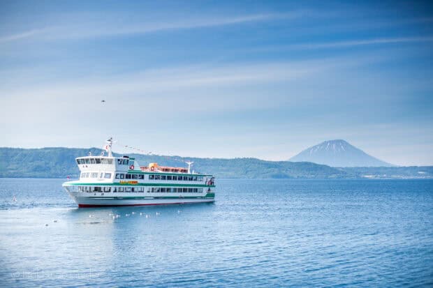 A ferry cruising on calm blue waters near a mountainous shoreline under a clear sky with Ferry Wallpapers, 2K Desktop Wallpaper