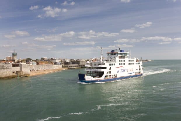 A ferry sails close to the coast with buildings in the background under a partly cloudy sky, 2K Desktop Wallpaper