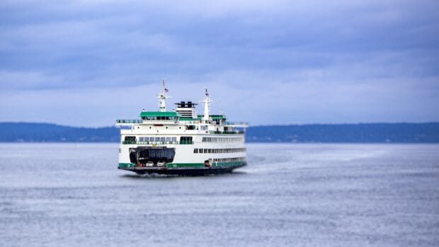 A ferry sailing on calm water under a cloudy sky with distant shoreline, 4K Desktop Wallpaper