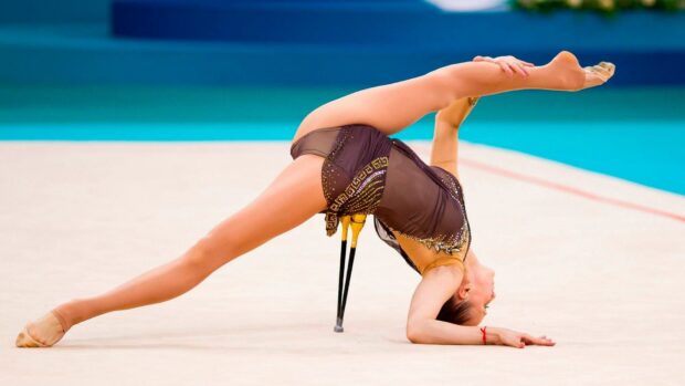 A gymnast demonstrates a flexible pose on the floor during an acrobatic gymnastics routine, HD Desktop Wallpaper