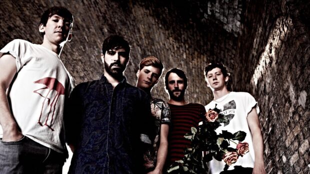 The Foals Band stands against a textured tunnel wall with roses in the foreground, HD Desktop Wallpaper