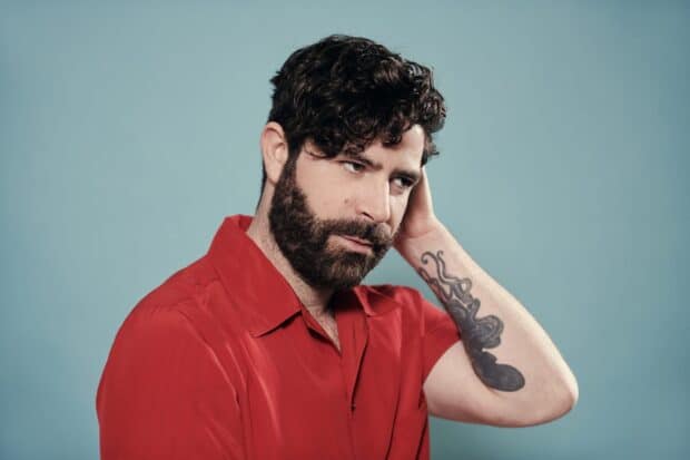 A man with curly hair and a tattoo on his arm is wearing a red shirt in this Foals Band Wallpapers photo, 2K Desktop Wallpaper