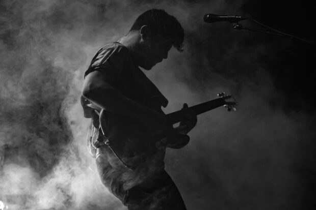 A talented Foals band member is playing guitar surrounded by smoky atmosphere, HD Desktop Wallpaper