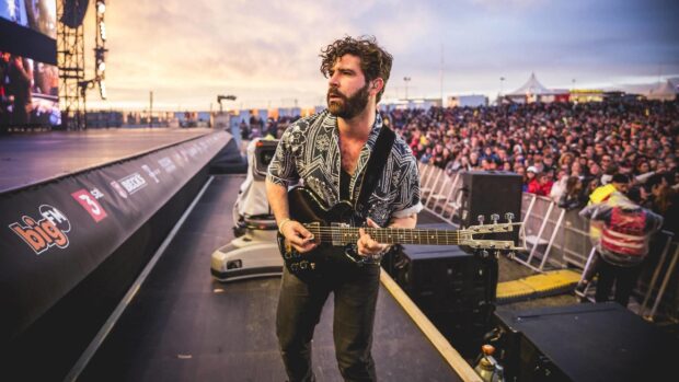 A Foals band guitarist plays an electric guitar during a live concert in front of a large crowd, 2K Desktop Wallpaper