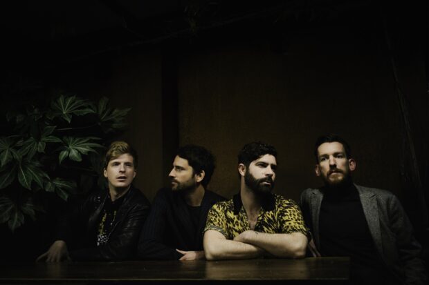 The Foals band members sit at a table with serious expressions, HD Desktop Wallpaper