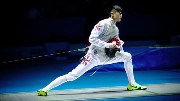 A fencing athlete with full gear lunges forward during a match on a blue floor, 2K Desktop Wallpaper