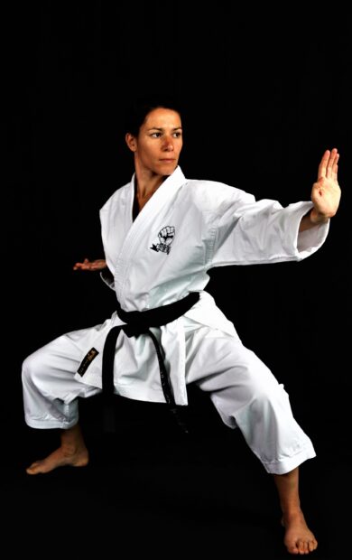 A woman demonstrates a focused karate stance wearing a black belt and white uniform, 2K Mobile Wallpaper