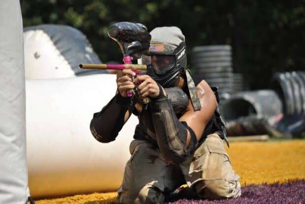 A paintball player is crouched and aiming his marker during a match on the field, HD Desktop Wallpaper