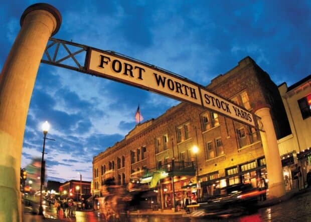 The Fort Worth Stockyards sign glows over the entrance with people and horses passing by at dusk, HD Desktop Wallpaper