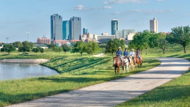A group of riders on horses riding along a path with the Fort Worth skyline in the background, HD Desktop Wallpaper
