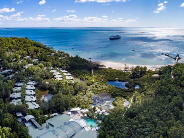 An aerial view shows Fraser Island with lush greenery and boats on the water, 2K Desktop Wallpaper
