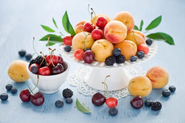 A plate full of fresh apricot and various berries sits on a table with some scattered around it, HD Desktop Wallpaper