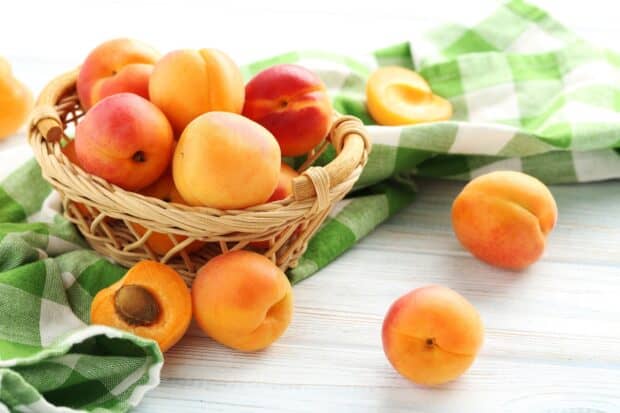 A wicker basket filled with fresh apricots on a wooden table with a green cloth, HD Desktop Wallpaper