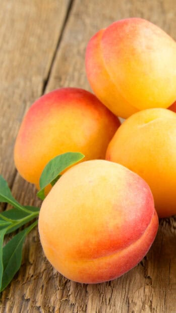 Fresh apricot fruit with green leaves resting on a wooden surface in natural light, HD Mobile Wallpaper