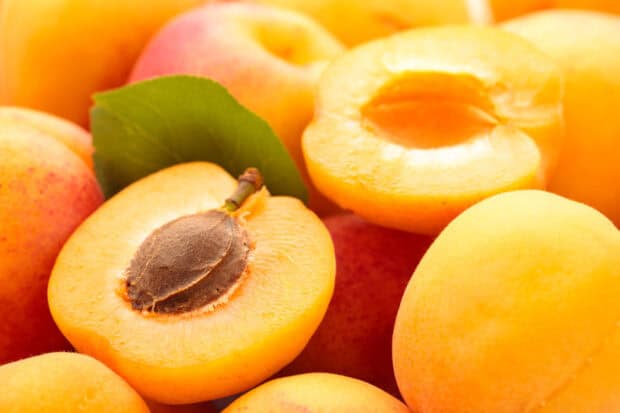 A close up of fresh apricot fruit showing the seed and leaf on a vibrant orange background, HD Desktop Wallpaper