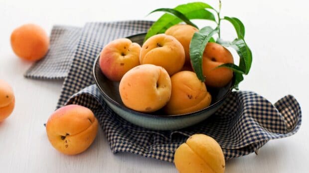Fresh apricot fruits arranged in a bowl on a cloth with green leaves, HD Desktop Wallpaper