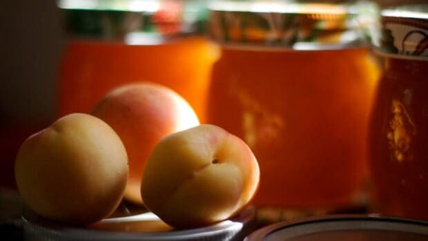Fresh apricot fruits placed on a kitchen surface with jars in the background, 2K Desktop Wallpaper