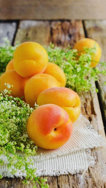 Fresh apricot fruits are placed on a wooden table with green flowers and a white cloth, HD Mobile Wallpaper