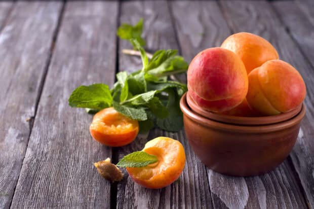 Fresh apricot fruits with green leaves placed on a wooden table with a bowl, HD Desktop Wallpaper