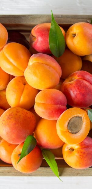 A close up of fresh apricots with green leaves arranged in a wooden crate, 2K Phone Wallpaper