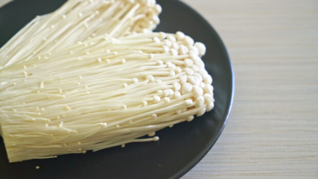 Fresh enoki mushrooms arranged neatly on a black plate on a light wooden surface, 4K Desktop Wallpaper