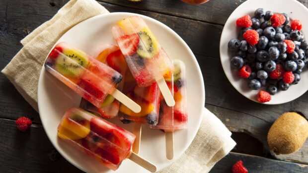 A plate of fresh fruit popsicles with kiwi and berries is placed on a wooden table, 4K Desktop Wallpaper